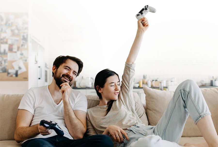 Couple holding game controllers on the couch laughing and cheering